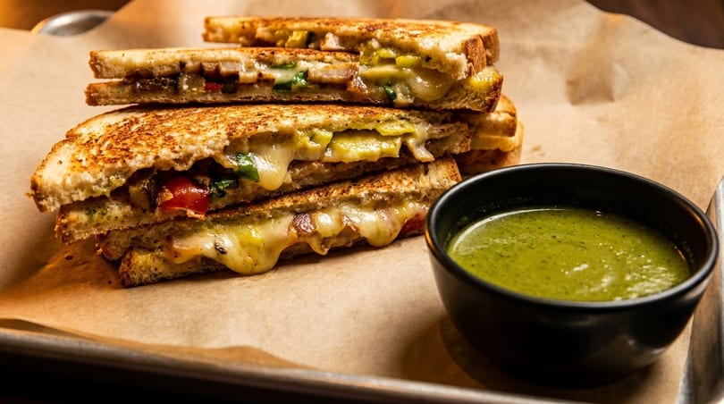 Grilled cheese sandwiches with melted cheese and vegetables, served with a side of green soup.