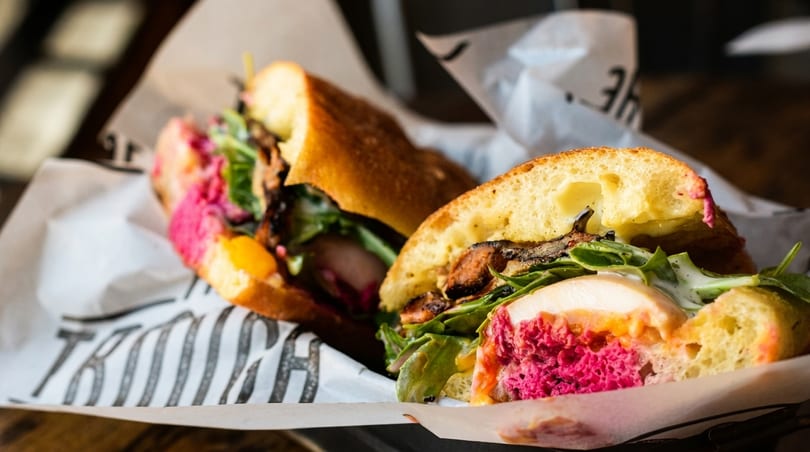 Two halves of a sandwich with chicken, bright pink beet spread, greens, and mushrooms.