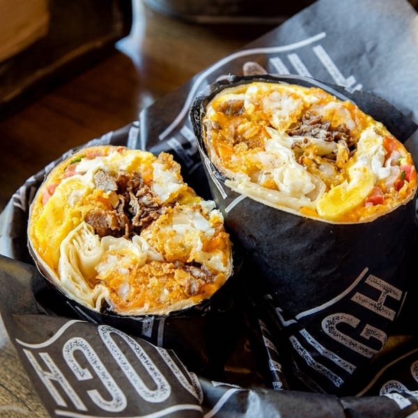 Two halves of a breakfast burrito filled with eggs, meat, and cheese, wrapped in branded paper.