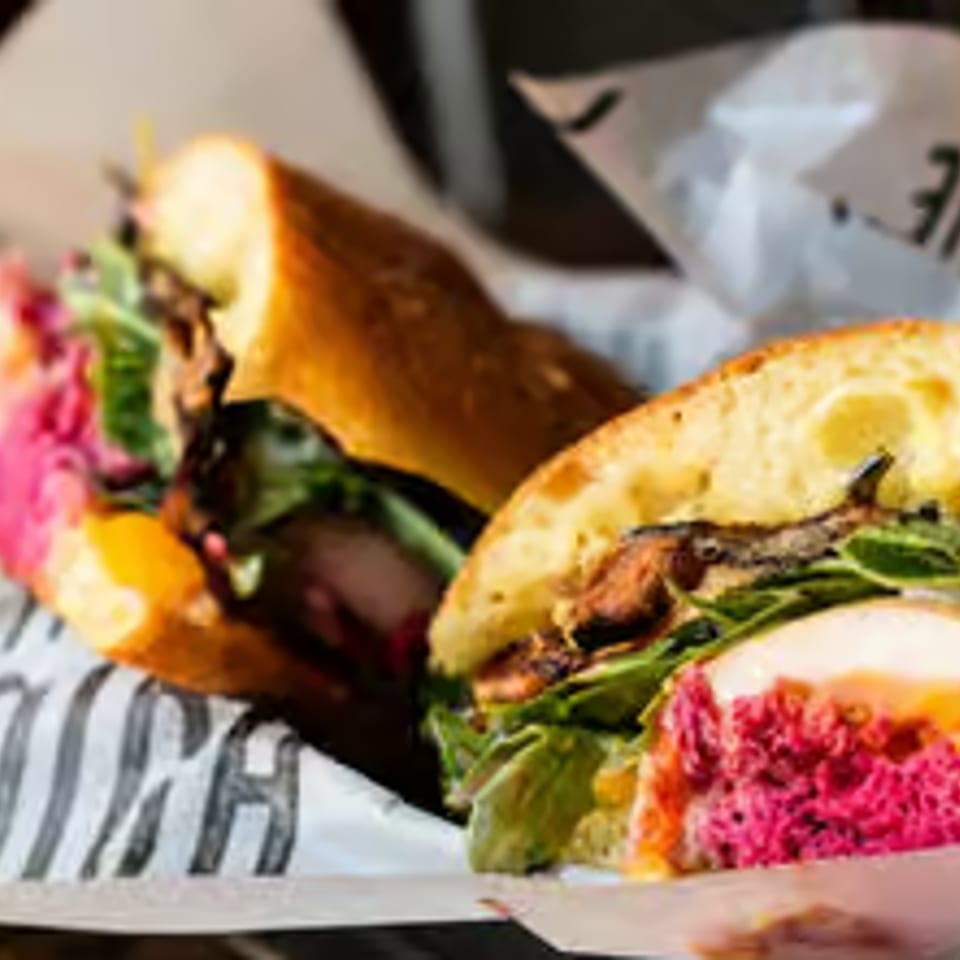 Two halves of a sandwich with pink filling, greens, and meat on a baguette.