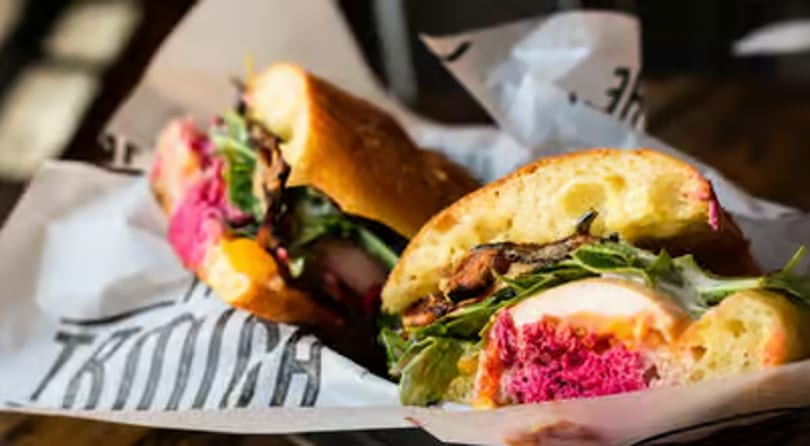 Two halves of a sandwich with pink filling, greens, and meat on a baguette.