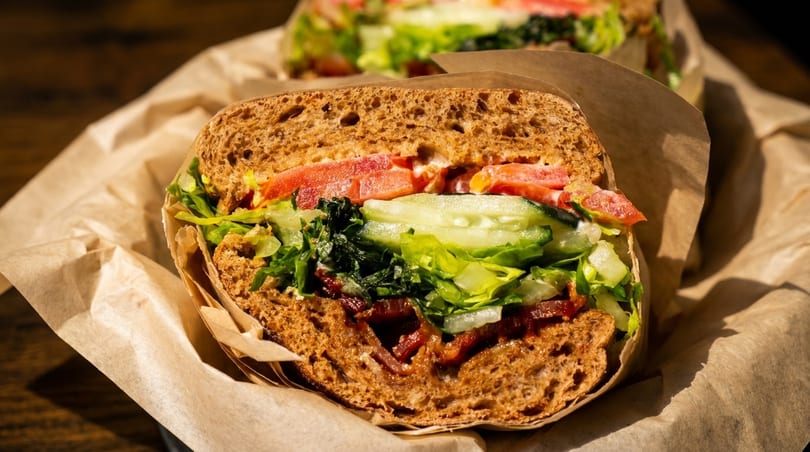 A close-up of a sandwich with bacon, lettuce, tomato, and cucumber on whole wheat bread.