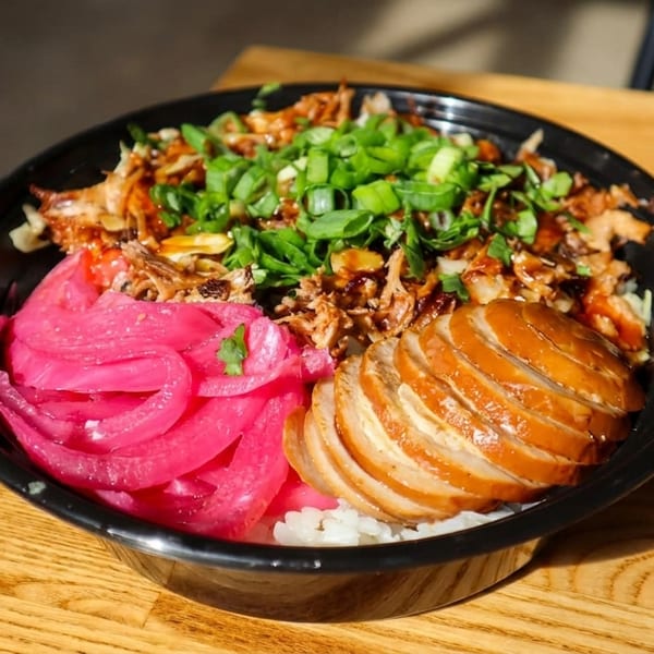 A colorful rice bowl with sliced chicken, pulled pork, pickled red onions, and green onions.