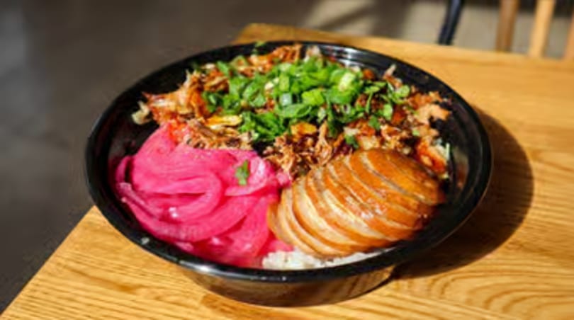 A bowl of rice topped with shredded meat, sliced meat, pickled red onions, and green onions.