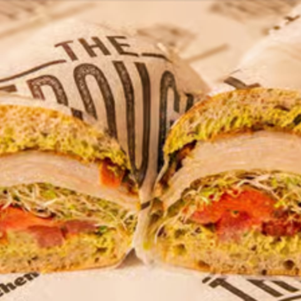 A turkey sandwich cut in half, revealing sprouts, tomatoes, and pesto on artisan bread.