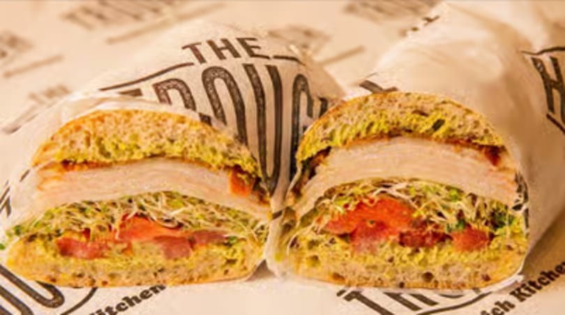 A turkey sandwich cut in half, revealing sprouts, tomatoes, and pesto on artisan bread.
